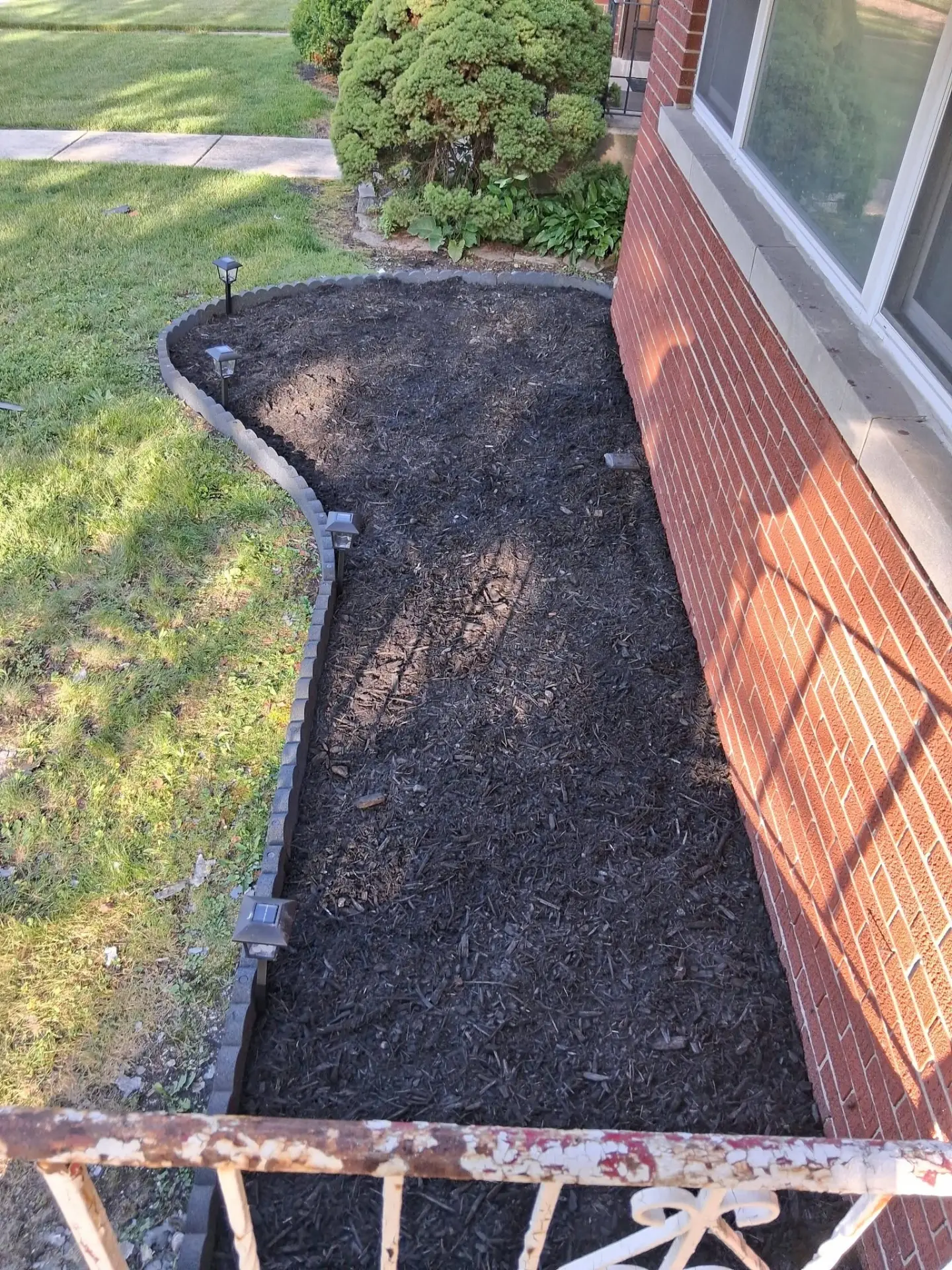 Freshly mulched landscaping bed with new edging beside a brick home